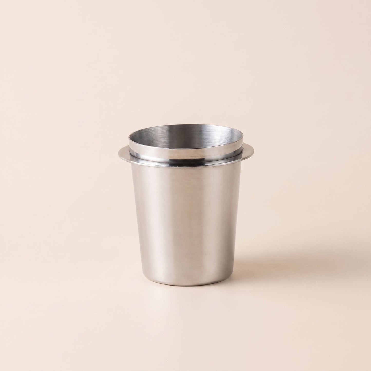 Glossy mirror-polished stainless dosing cup, front three-quarter view on a cream background