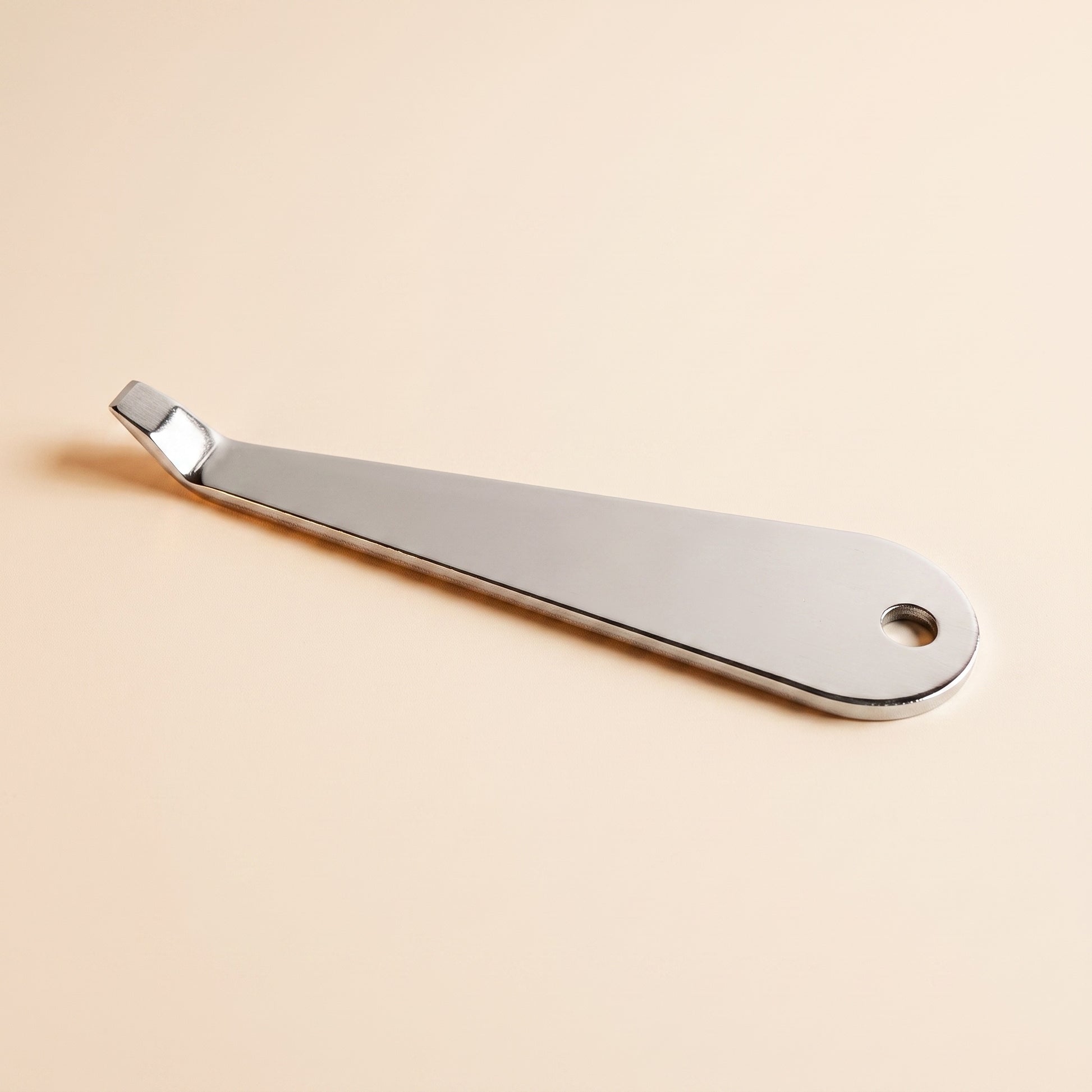 Stainless portafilter basket removal tool on flat cream background, front view, polished steel with hook tip