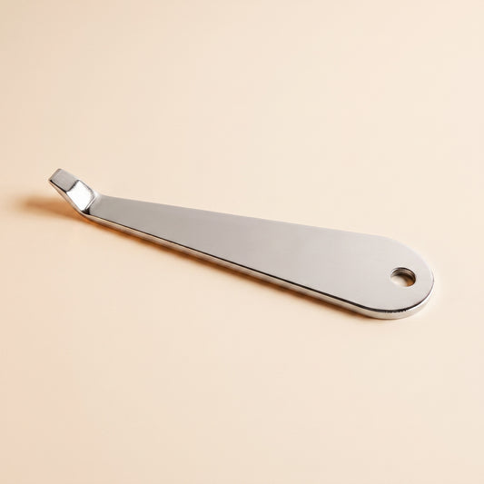 Stainless portafilter basket removal tool on flat cream background, front view, polished steel with hook tip