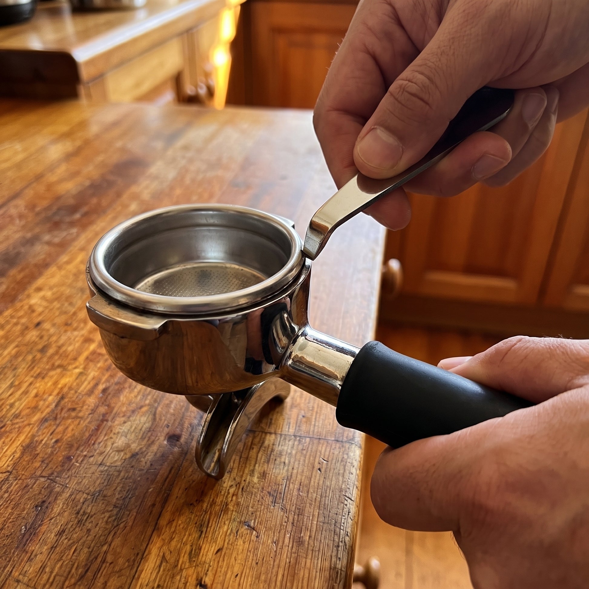 Portafilter basket removal tool in use, hooked tip lifting a basket from an espresso portafilter