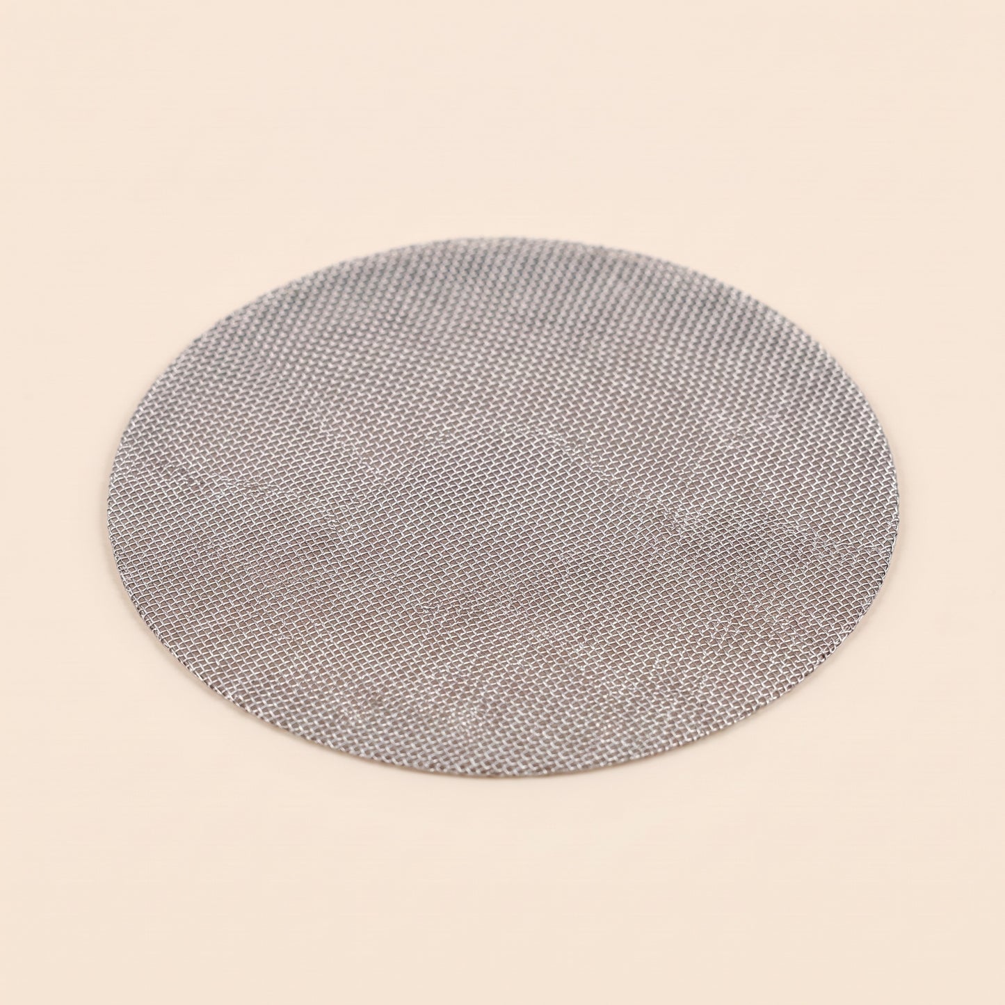 Reusable stainless mesh puck screen on flat cream background, front view, 150 micron