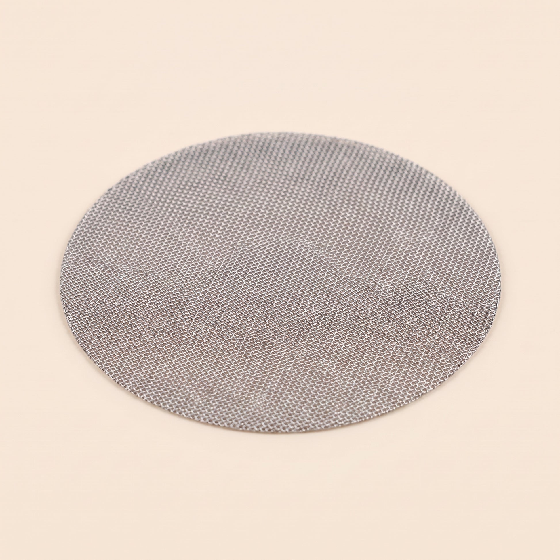 Reusable stainless mesh puck screen on flat cream background, front view, 150 micron